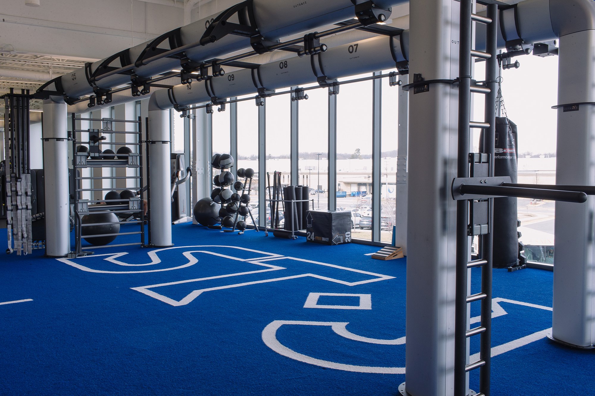 A functional training area at The St. James Northern Virginia, featuring a pull-up rig, medicine ball racks, a punching bag, and plyo boxes near floor-to-ceiling windows.